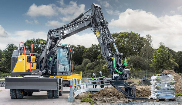 Volvo hydraulic excavator with long arm and breaker attachment at a construction site, workers in high-visibility vests nearby.